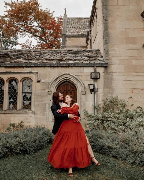 a man and a woman are dancing in front of a building . the woman is wearing a red dress . natural wedding makeup. pittsburgh, pa. bridal makeup. bridal mua. wedding makeup artist. moriah e beauty. AMC photography.