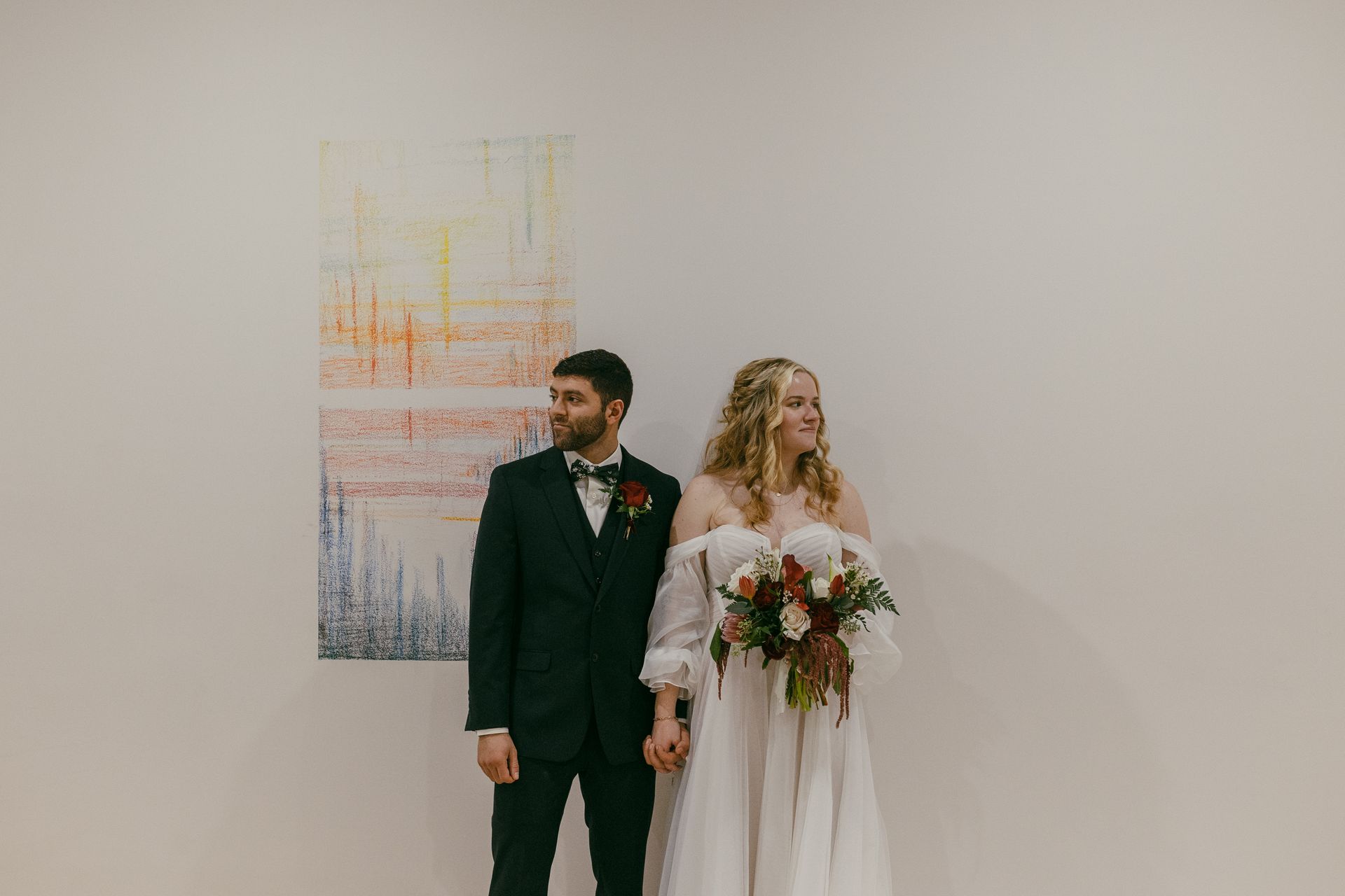 a bride and groom are holding hands in front of a painting on a wall . natural wedding makeup. pittsburgh, pa. bridal makeup. bridal mua. wedding makeup artist. moriah e beauty. hannah conti photography.