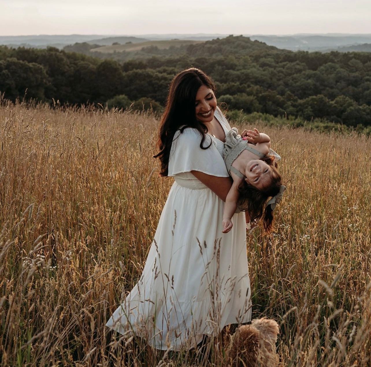 a woman in a white dress is holding a little girl in her arms in a field . natural makeup. pittsburgh, pa. family photos makeup. bridal mua. wedding makeup artist. moriah e beauty. kathy wolfe photography.