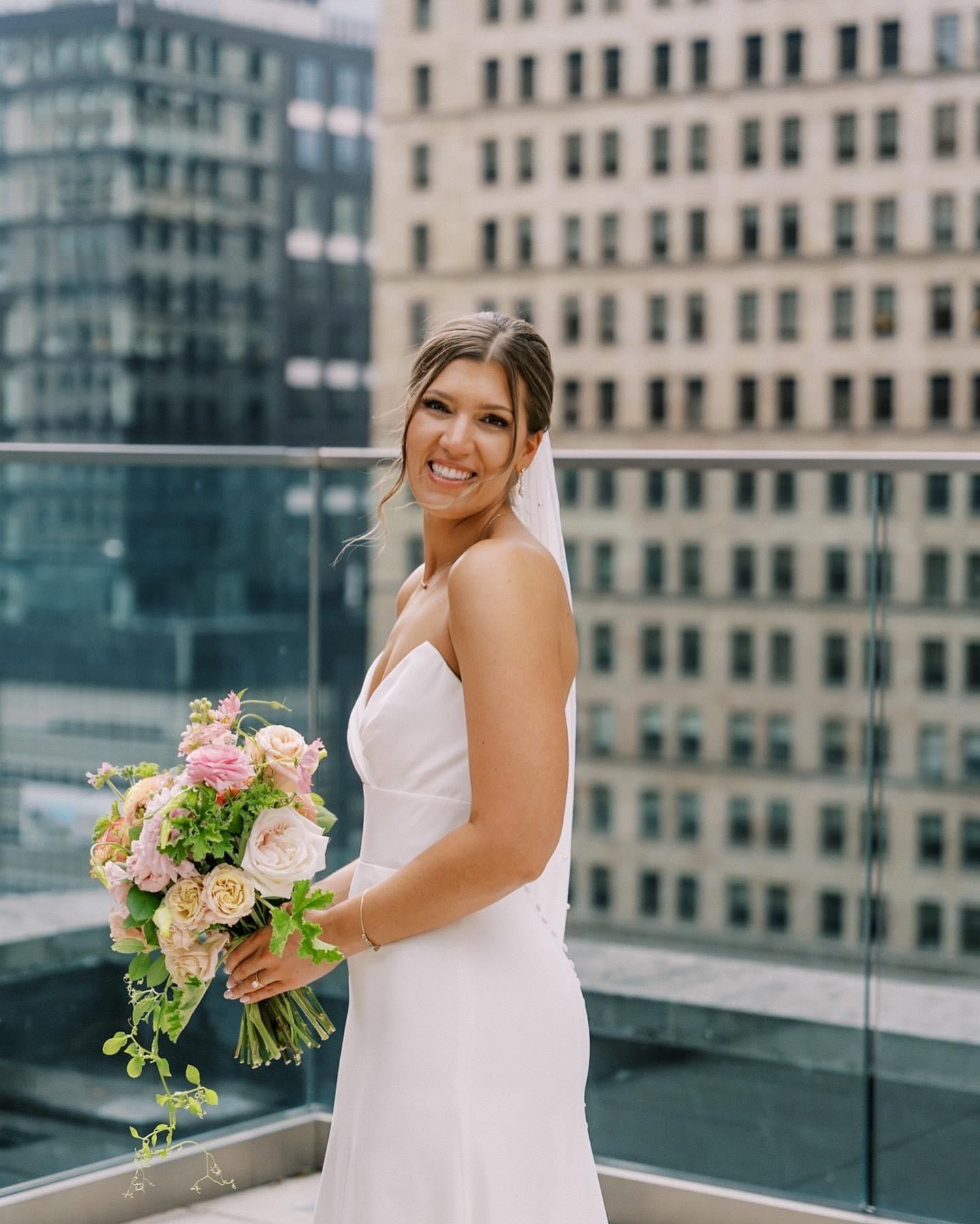 a bride in a white dress is holding a bouquet of flowers on a balcony . natural wedding makeup. pittsburgh, pa. bridal makeup. bridal mua. wedding makeup artist. moriah e beauty. sarah mccloskey photography.