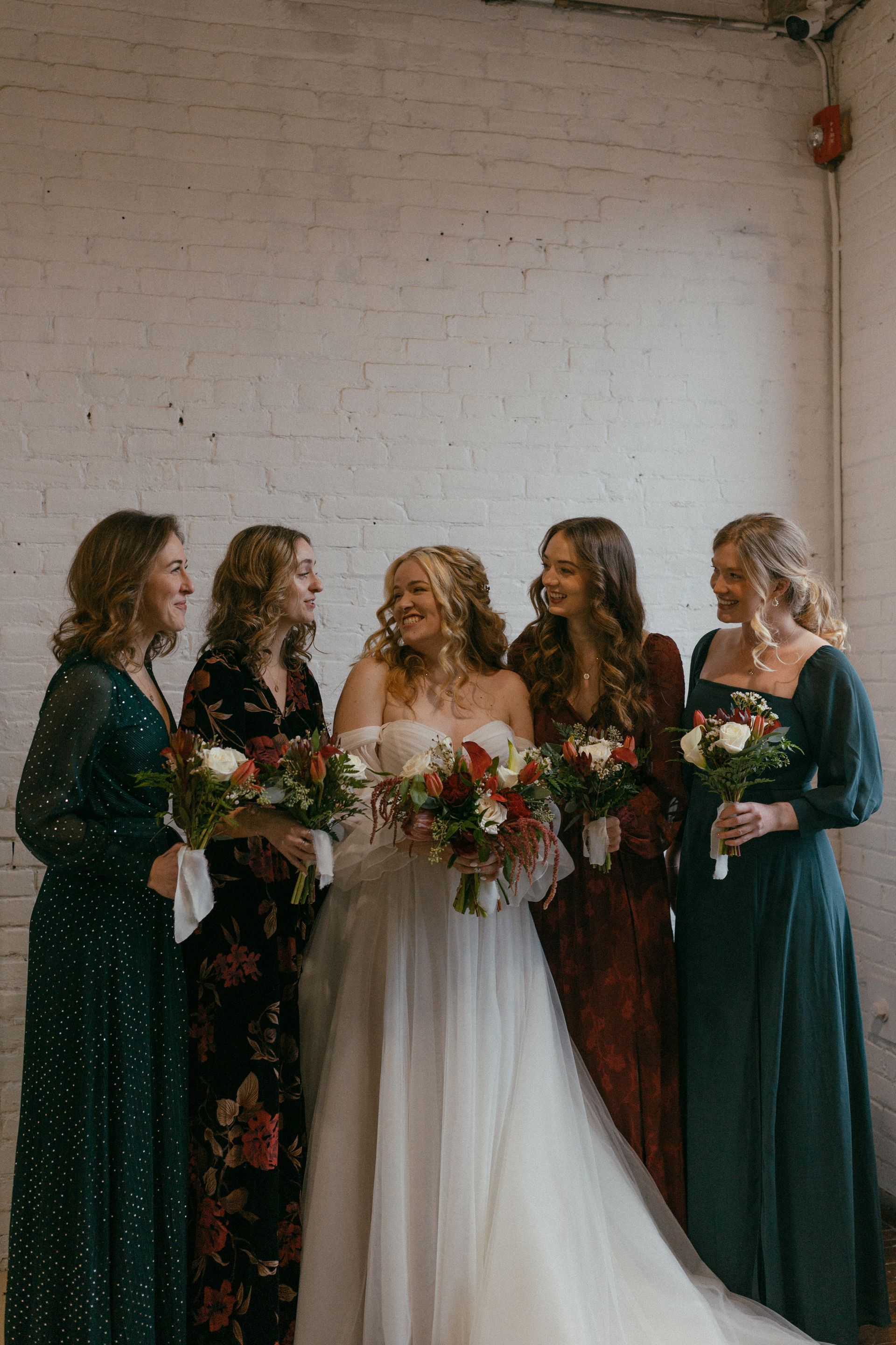 a bride and her bridesmaids are posing for a picture in front of a white brick wall . natural wedding makeup. pittsburgh, pa. bridal makeup. bridal mua. wedding makeup artist. moriah e beauty. hannah conti photography.