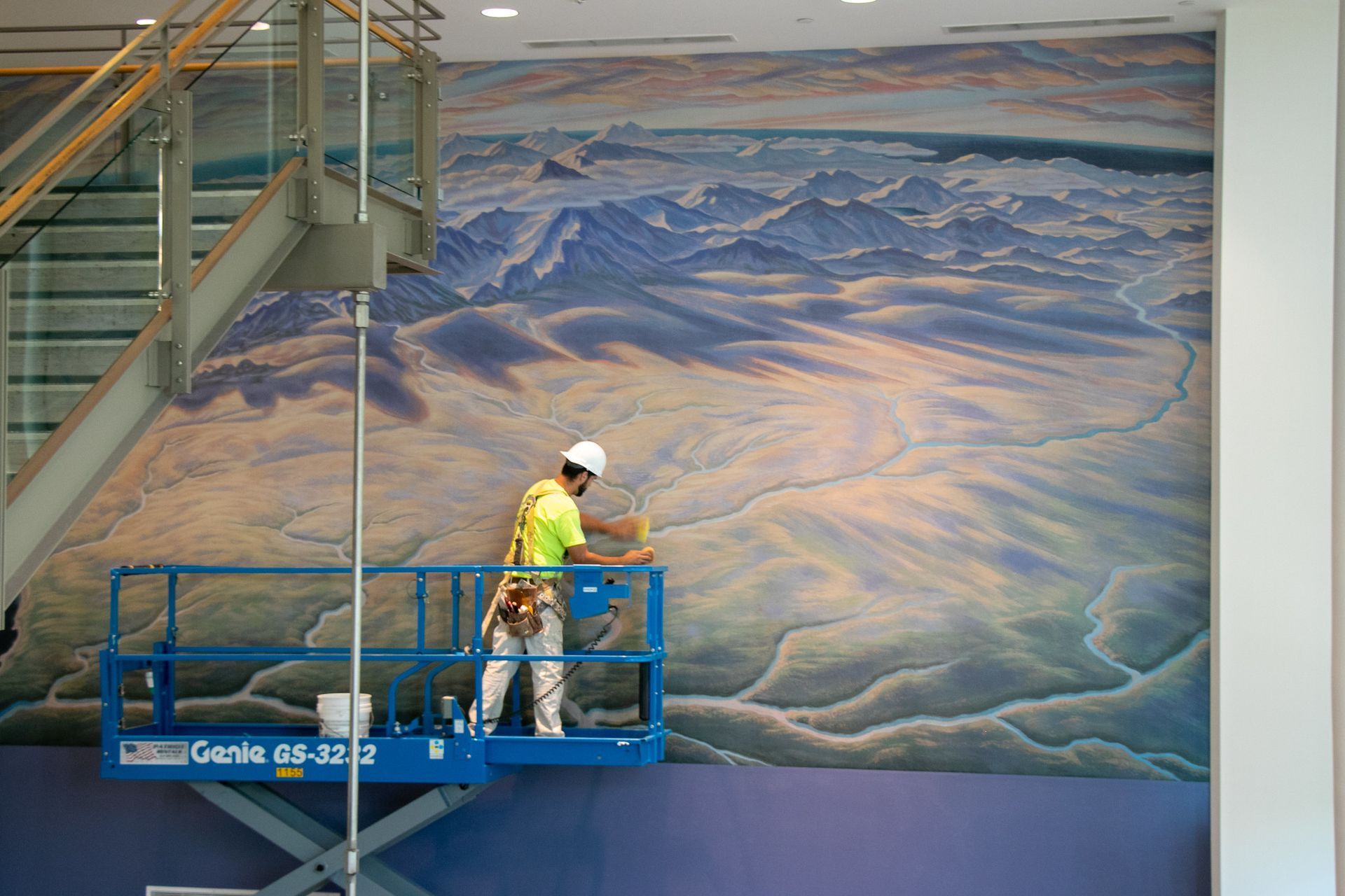 A man is standing on a lift painting a mural on a wall.