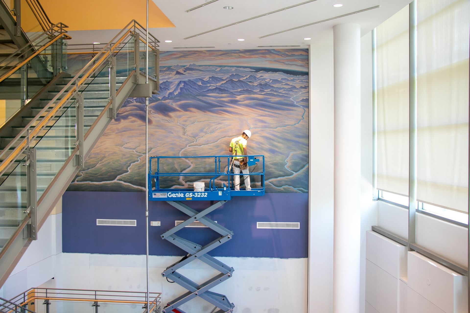 A man is standing on a scissor lift in front of a staircase