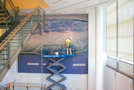 A man is standing on a scissor lift in front of a staircase