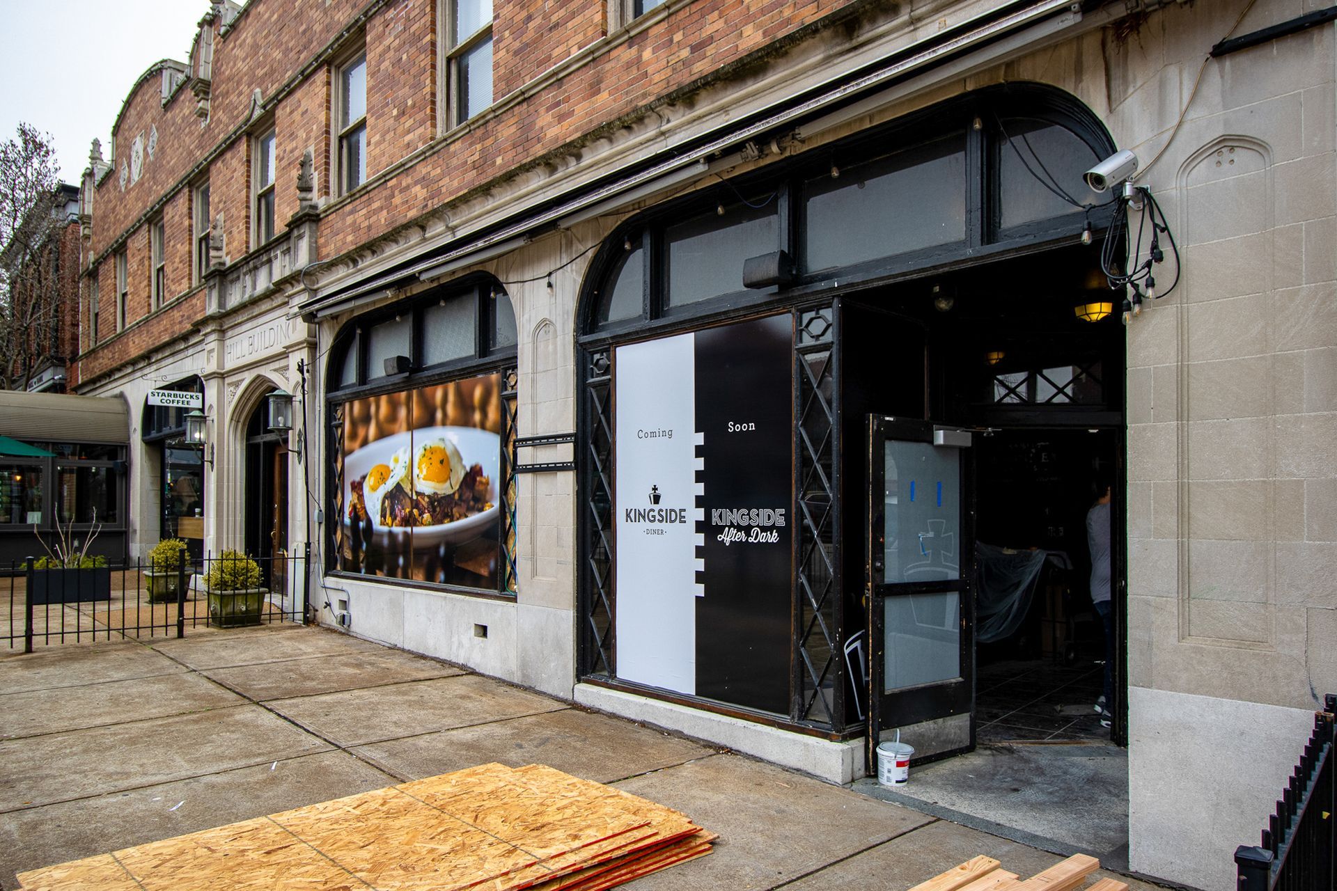Restaurant facade with black and white entrance, large windows, and a brick building. Sidewalk in front.