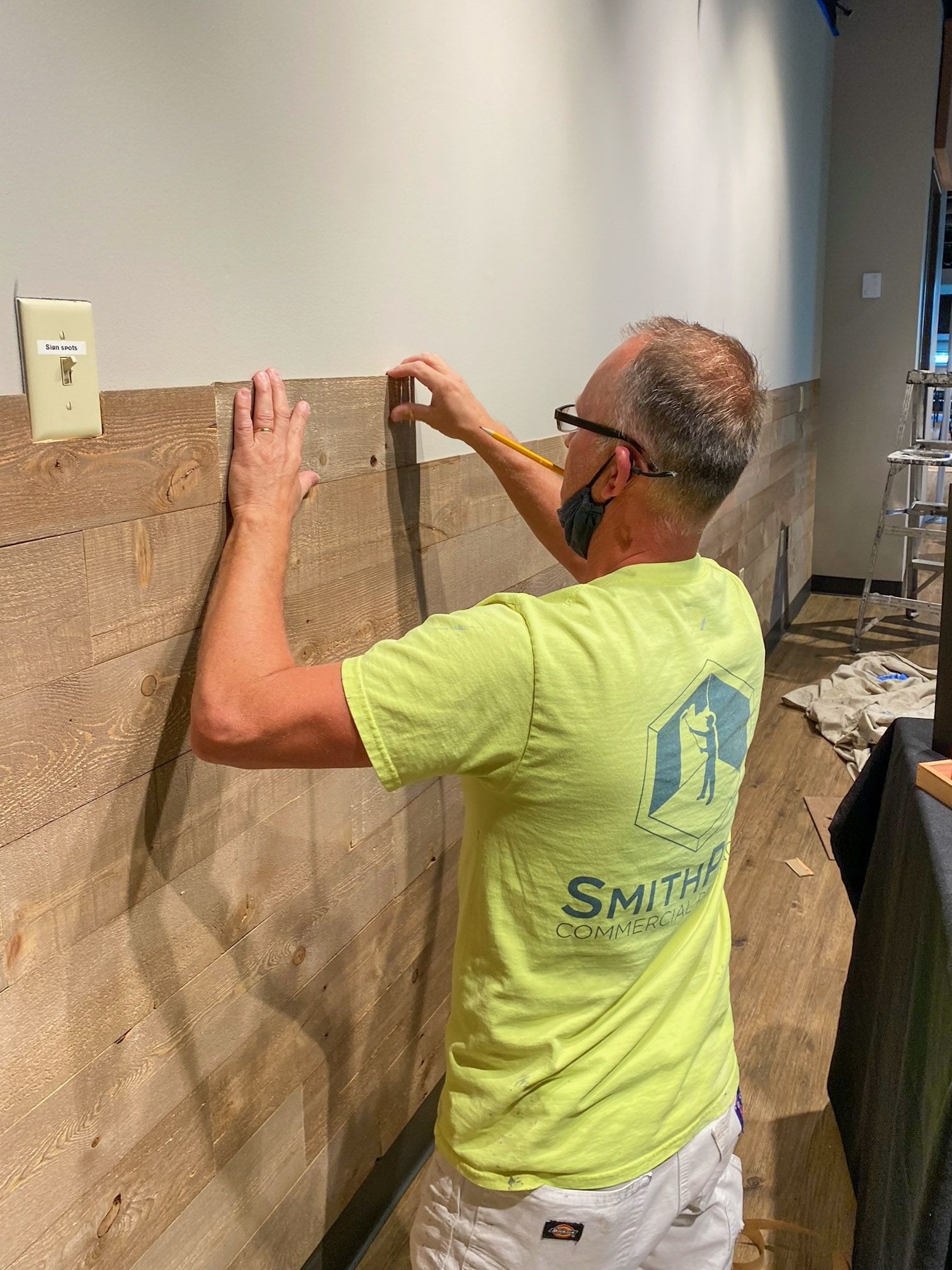 Man spraying paint with a professional airless sprayer wearing a respirator, in a room with a newly painted black wall.