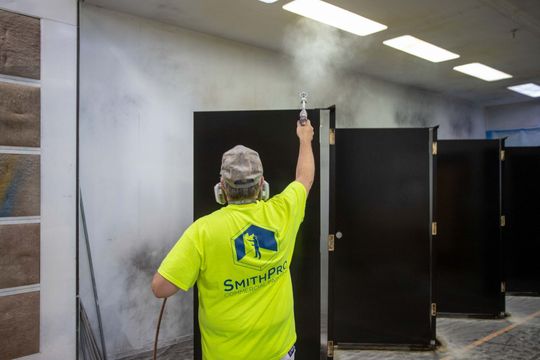 A man in a yellow shirt is spray painting a bathroom door.