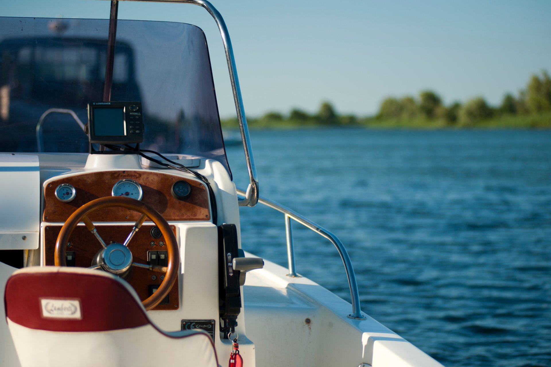Boat steering wheel and dashboard with a blue lake in the background.