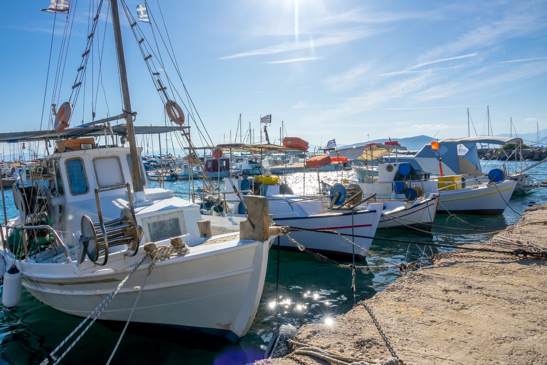 Fishing boats docked in a sunny harbor, blue water, clear sky.