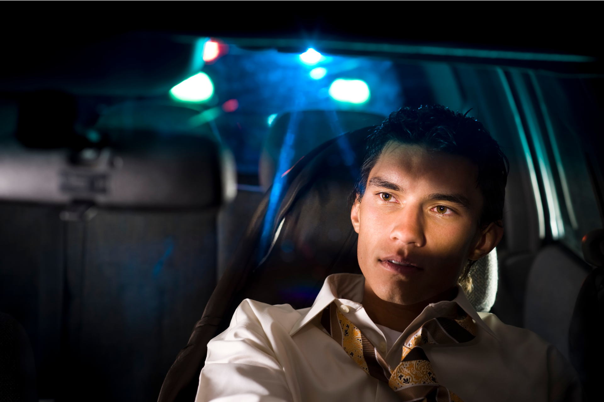 Man in car, looking to the side, illuminated by blue and green lights.