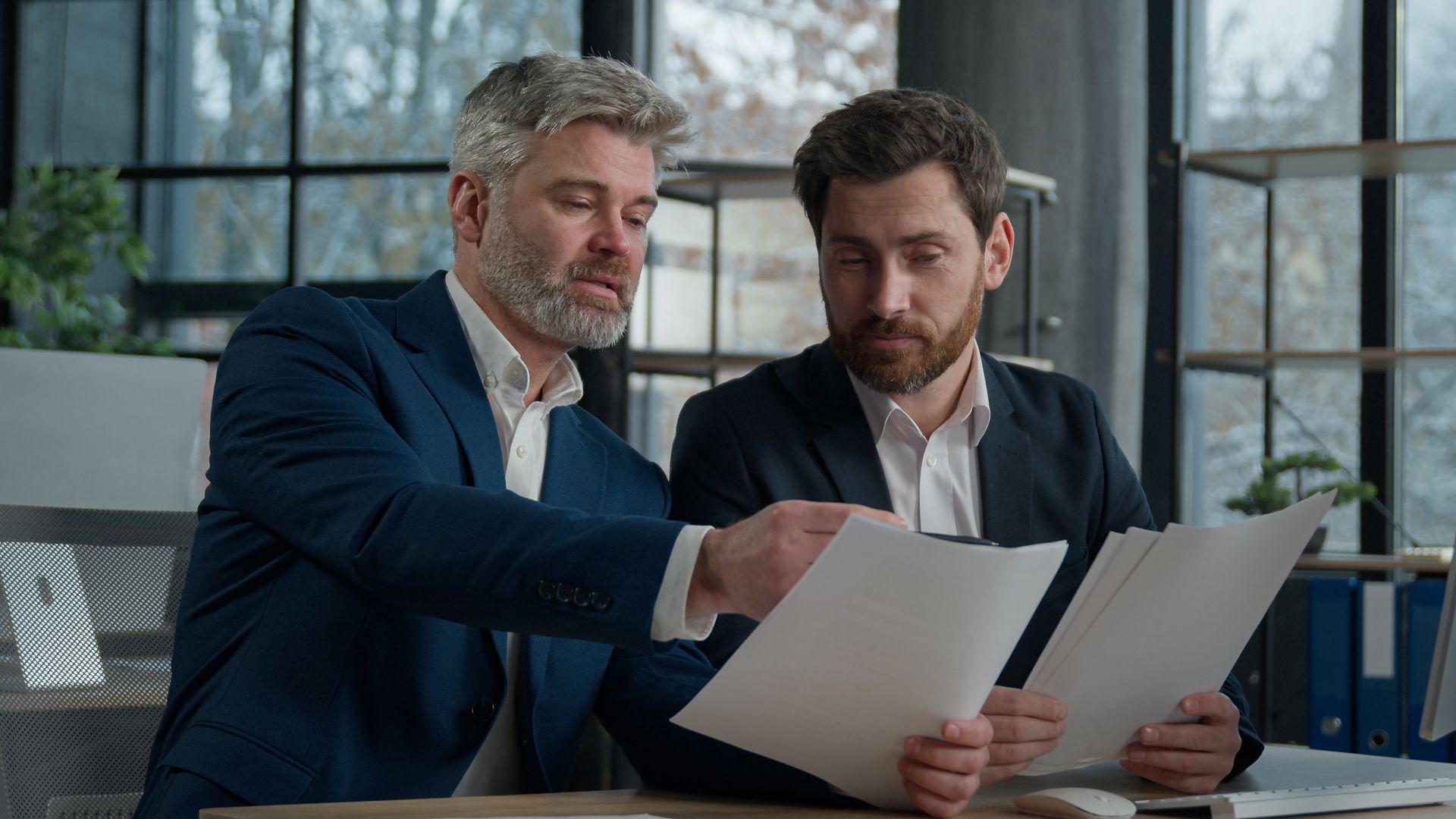 Two business professionals in suits reviewing documents, discussing strategy.