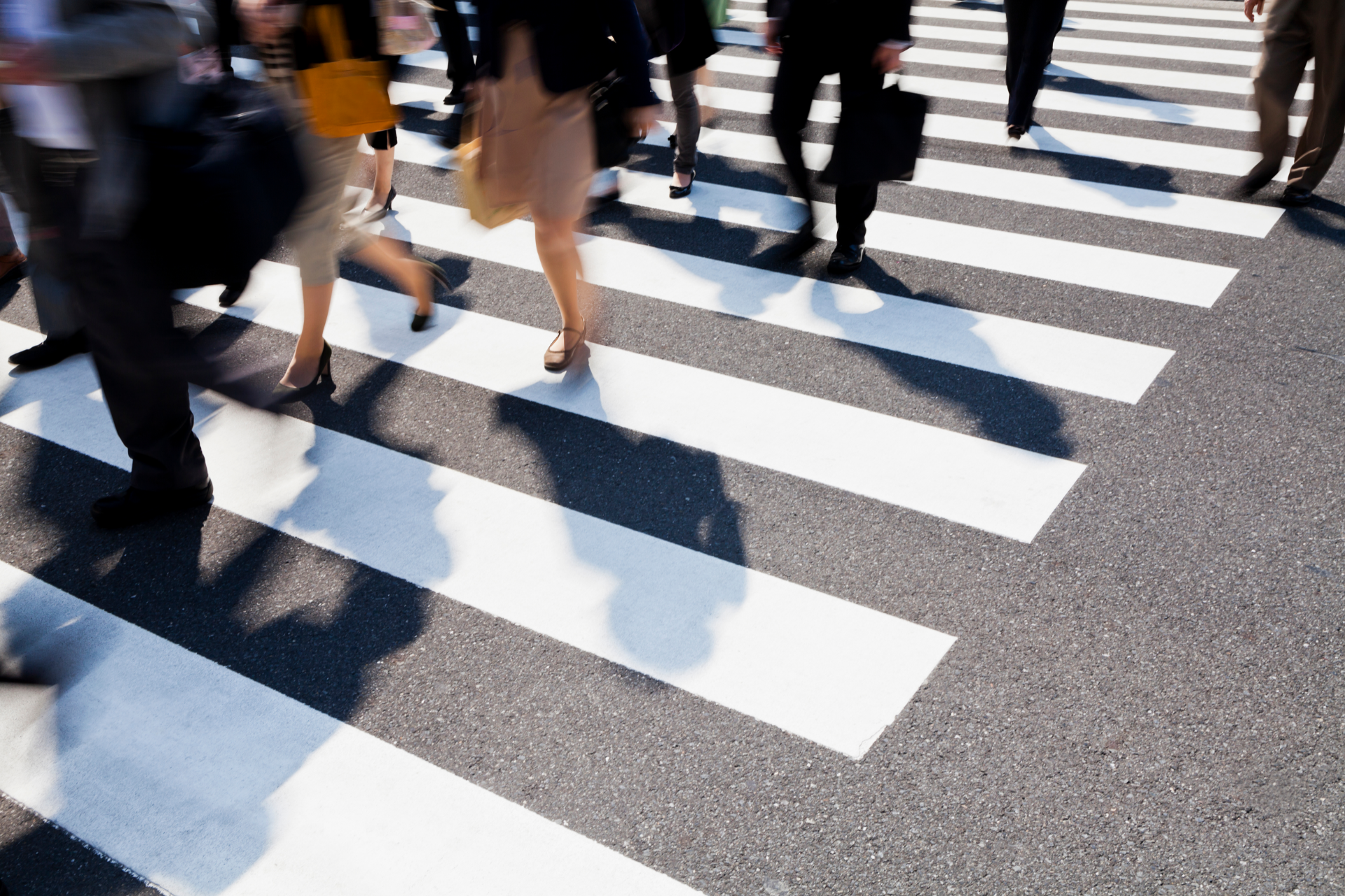 People walking on a zebra crossing in an urban setting; shadows cast by the sun.