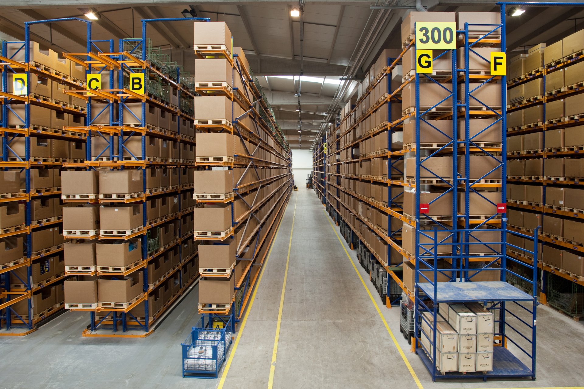 Warehouse interior with tall shelving packed with cardboard boxes, aisles, and overhead lighting.