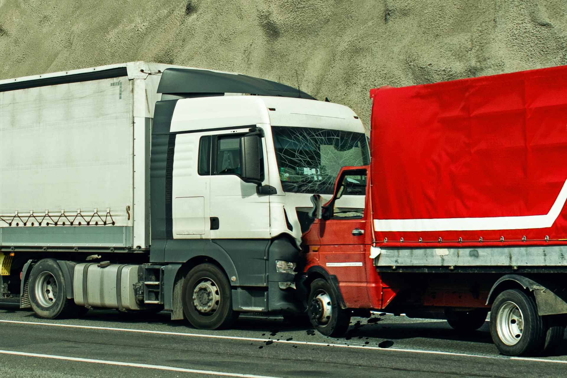 Two semi-trucks, white and red, collided on a highway. Debris visible on the road.