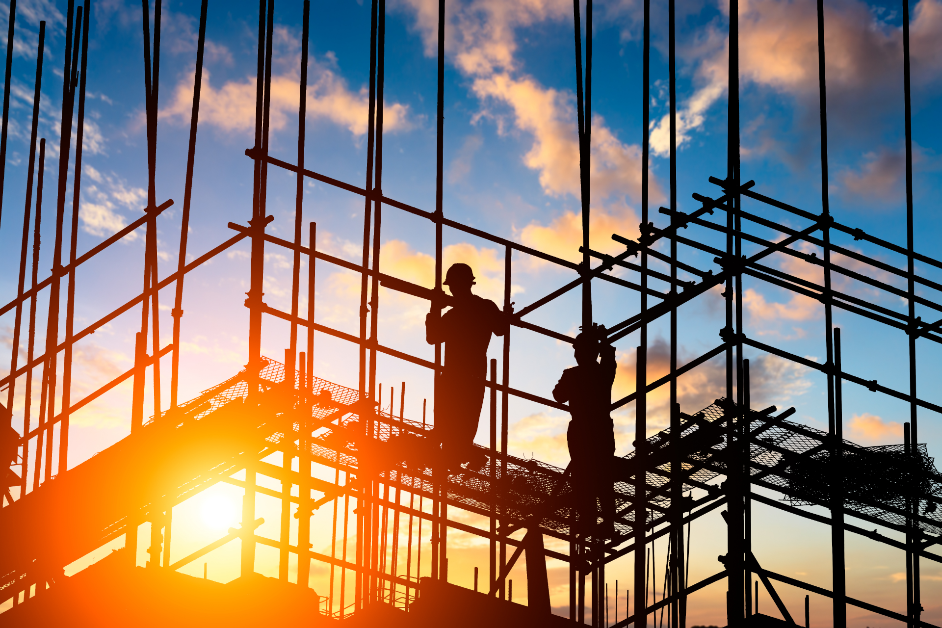 Construction workers silhouetted against a sunset, working on scaffolding.