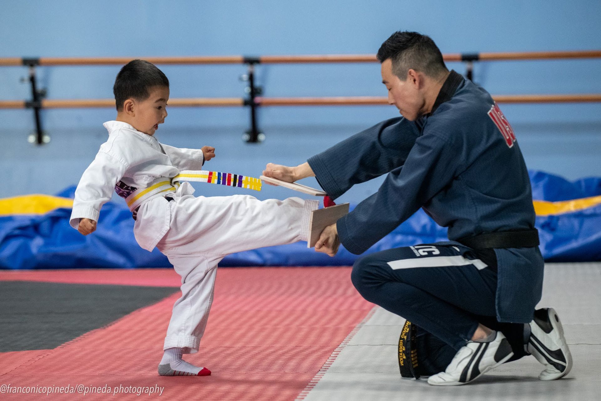 A man is kneeling down next to a young boy who is practicing karate.