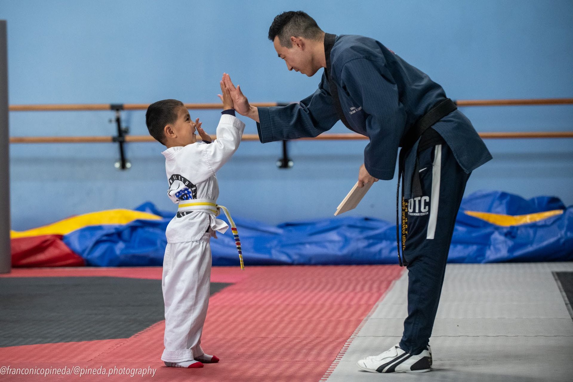 A man is giving a high five to a young boy in a karate uniform.