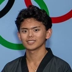 A young man is standing in front of a wall with olympic rings on it.