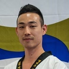 A man in a taekwondo uniform is standing in front of a flag.