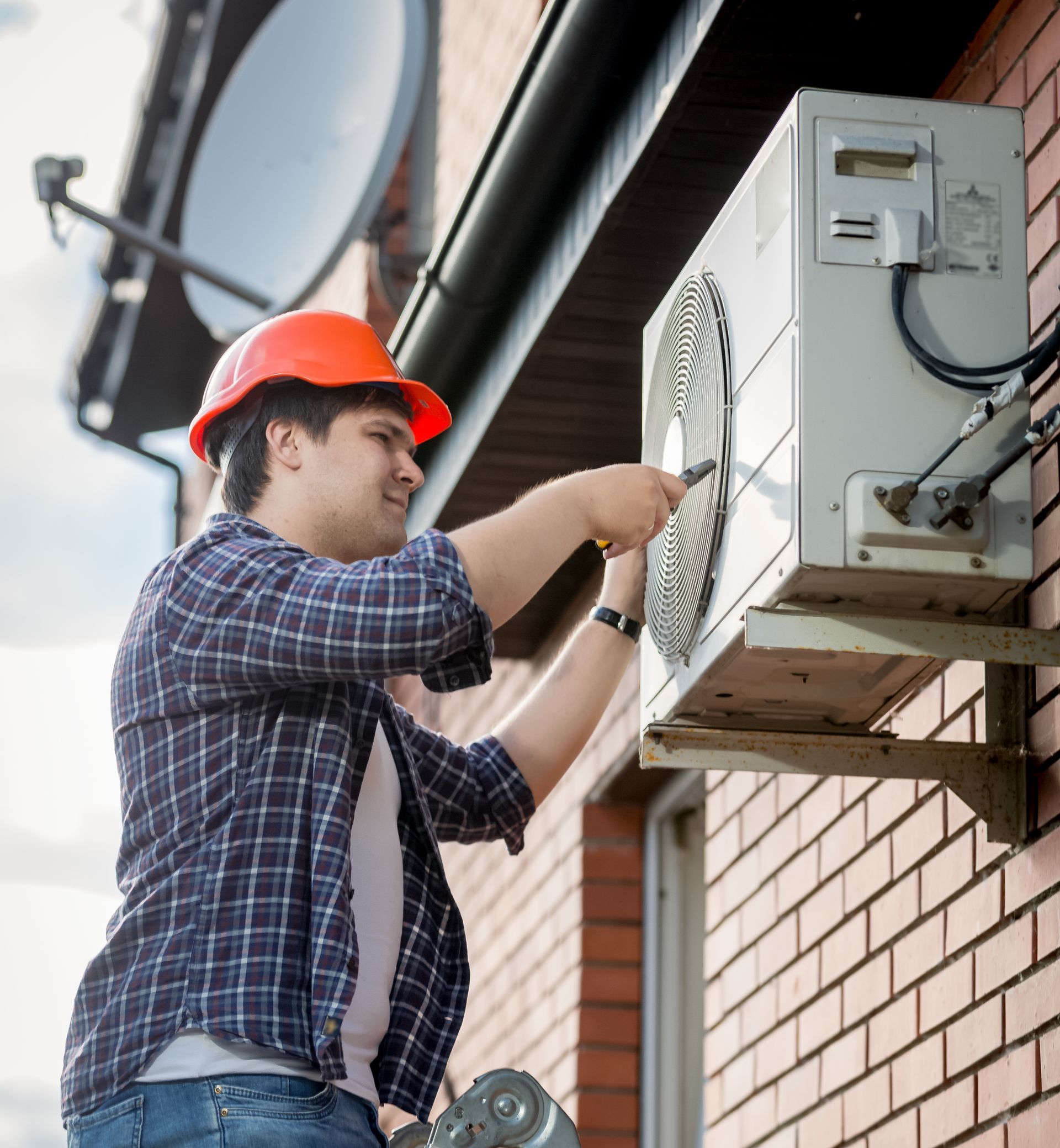 A man is working on an air conditioner on the side of a building.