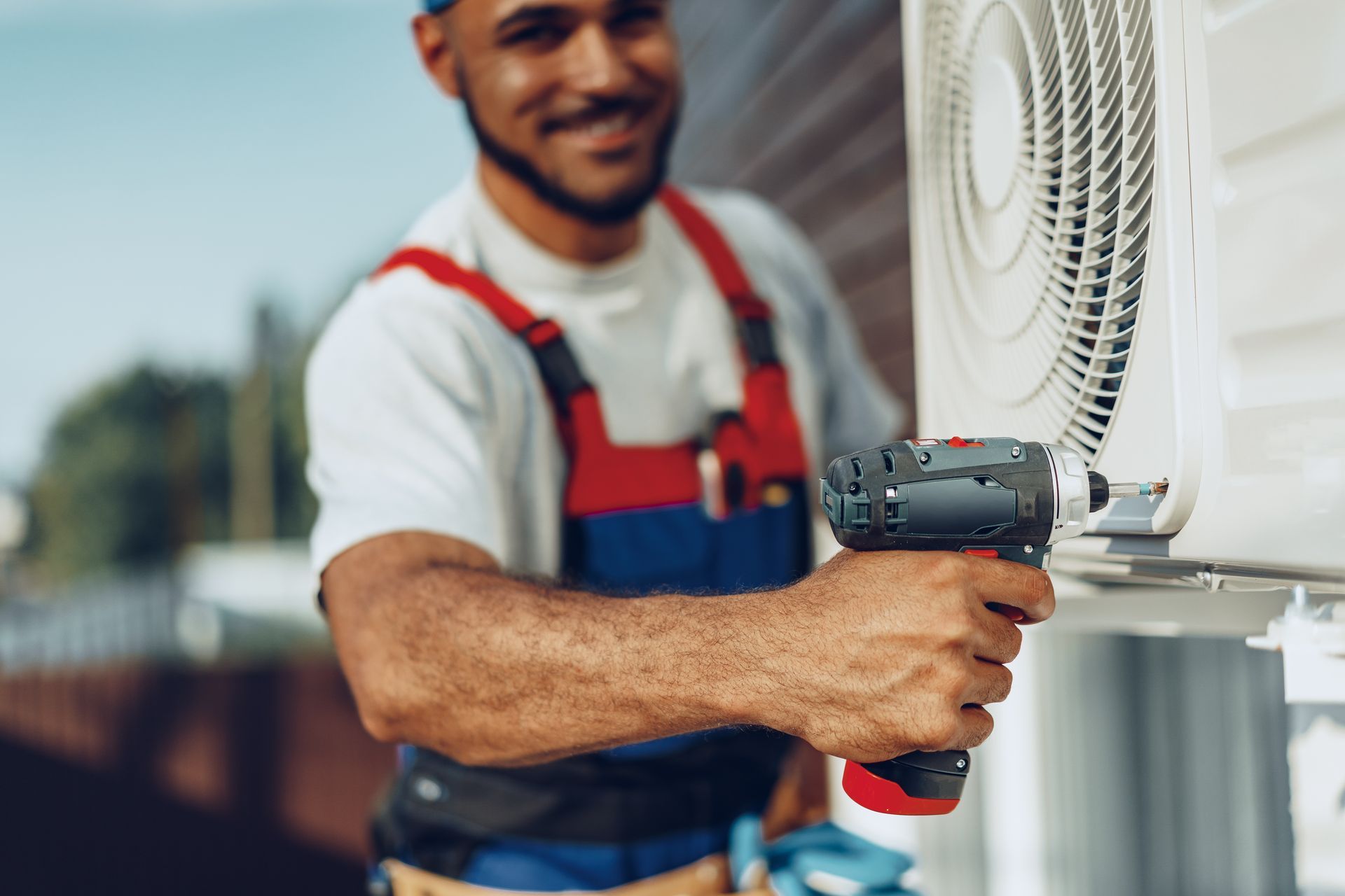 A man is using a drill to fix an air conditioner.