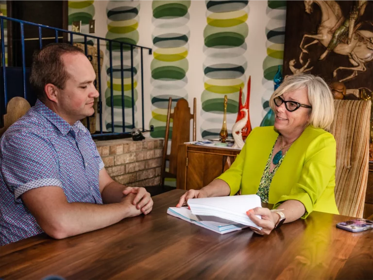 Man and woman seated at a table, reviewing documents. Woman in lime green jacket.