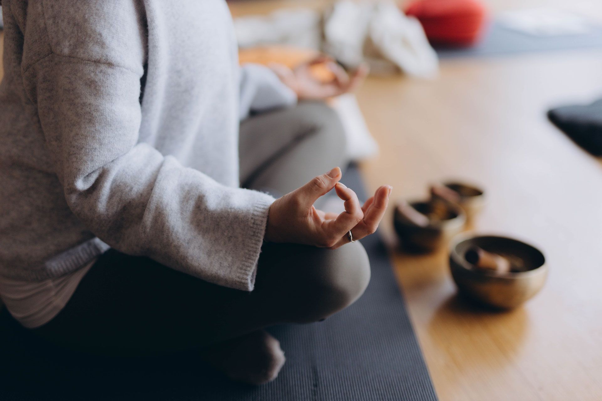 Person meditating, hands in mudra, seated on a mat, near singing bowls.