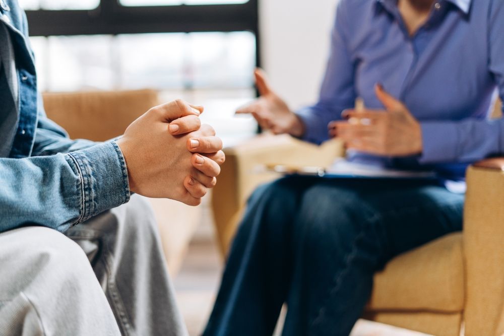 talking to person gesturing with hands while holding a clipboard in a well-lit room.