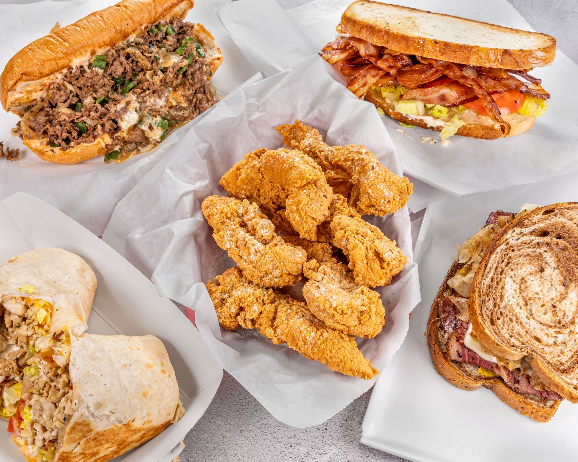 A variety of sandwiches and fried chicken are on a table.