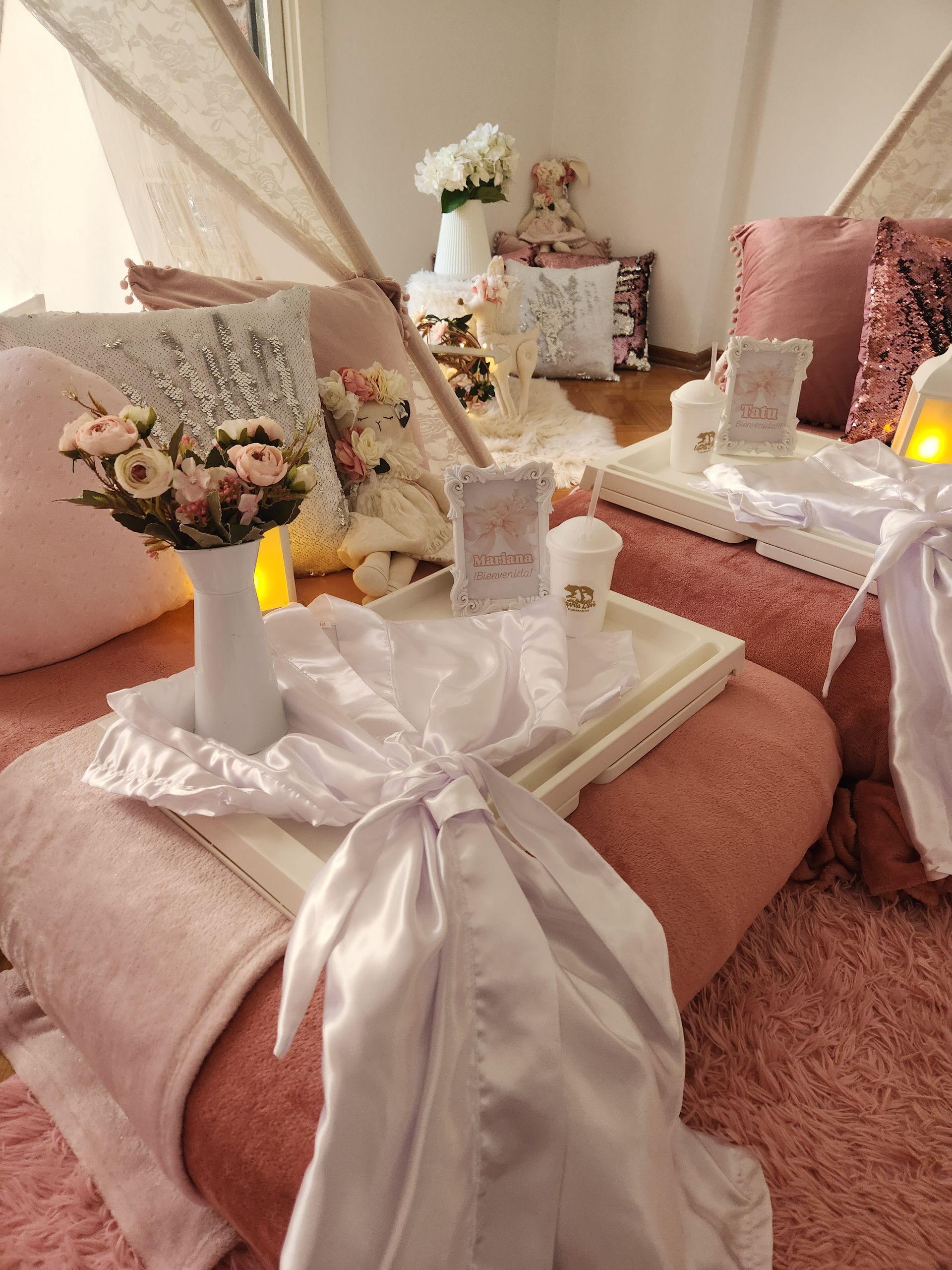 Un acogedor interior con temática rosa. Incluye cojines, flores, una bata blanca y una estructura tipo tipi.