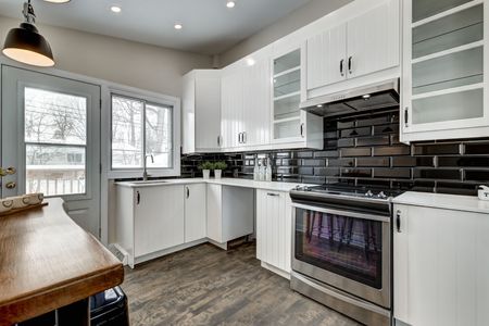 A kitchen with white cabinets , stainless steel appliances , and black tiles.