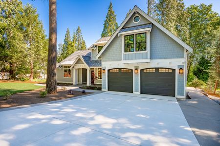 A large house with two garage doors is surrounded by trees and a concrete driveway.