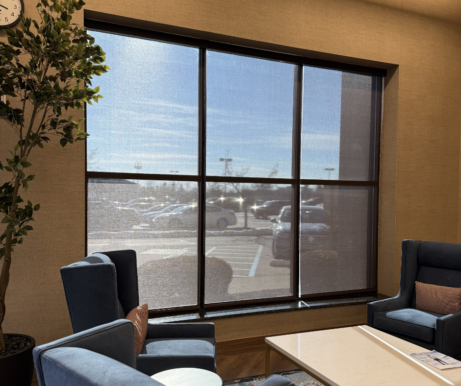 A seating area with blue armchairs, a table, and a large window looking out onto a parking lot.