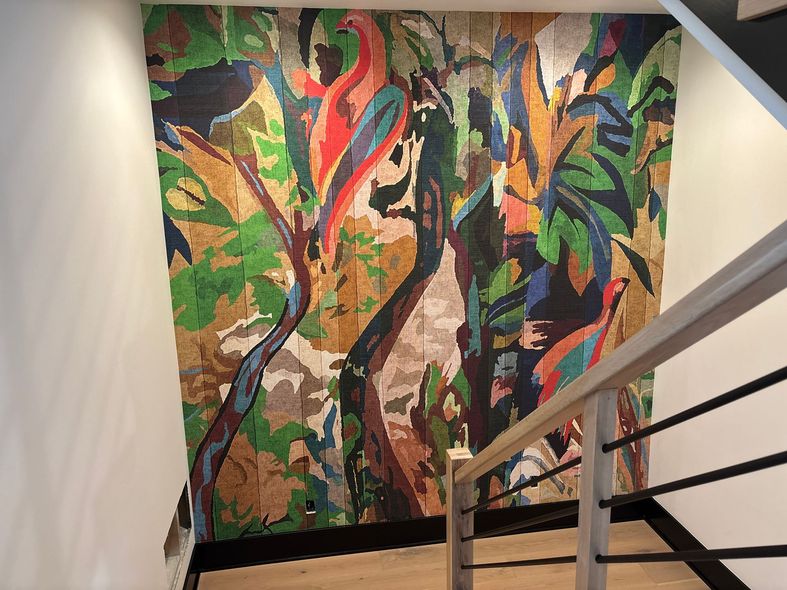 Colorful jungle mural on a stairwell wall beside a metal handrail.