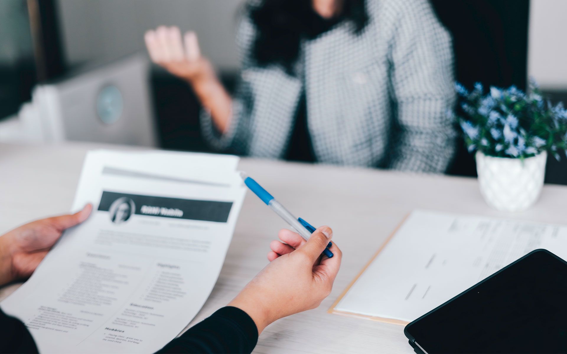 A woman is sitting at a desk with a pen and a resume.