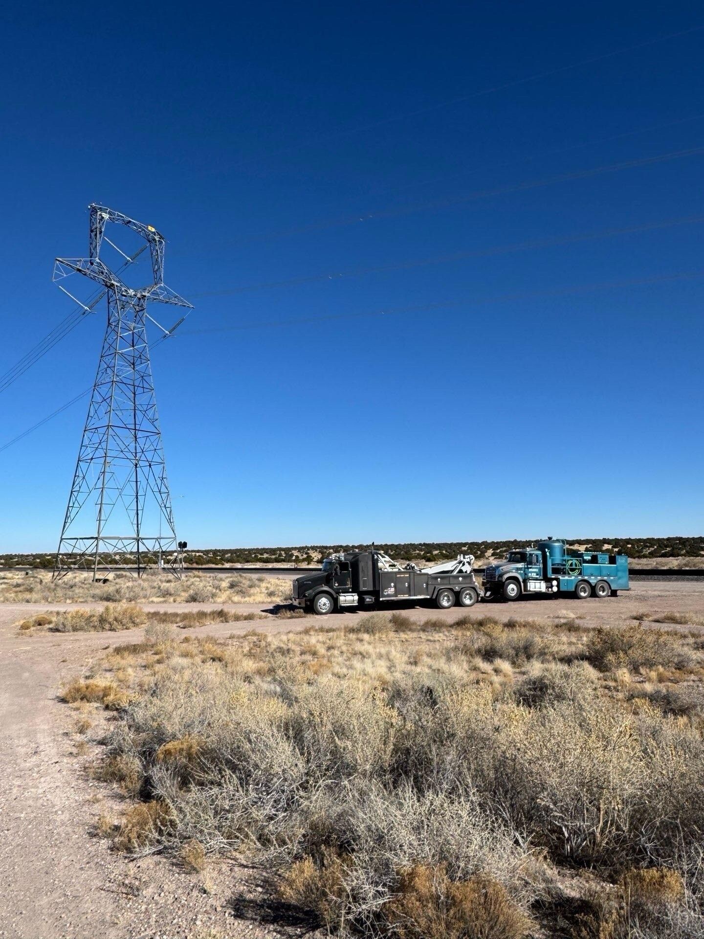 A truck is driving down a dirt road next to a power tower.