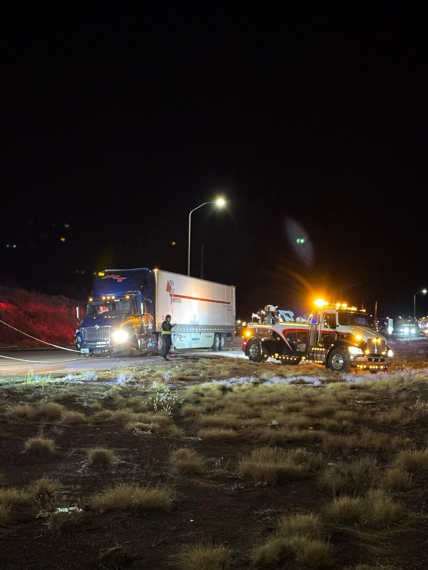 A semi truck is being towed by a tow truck at night