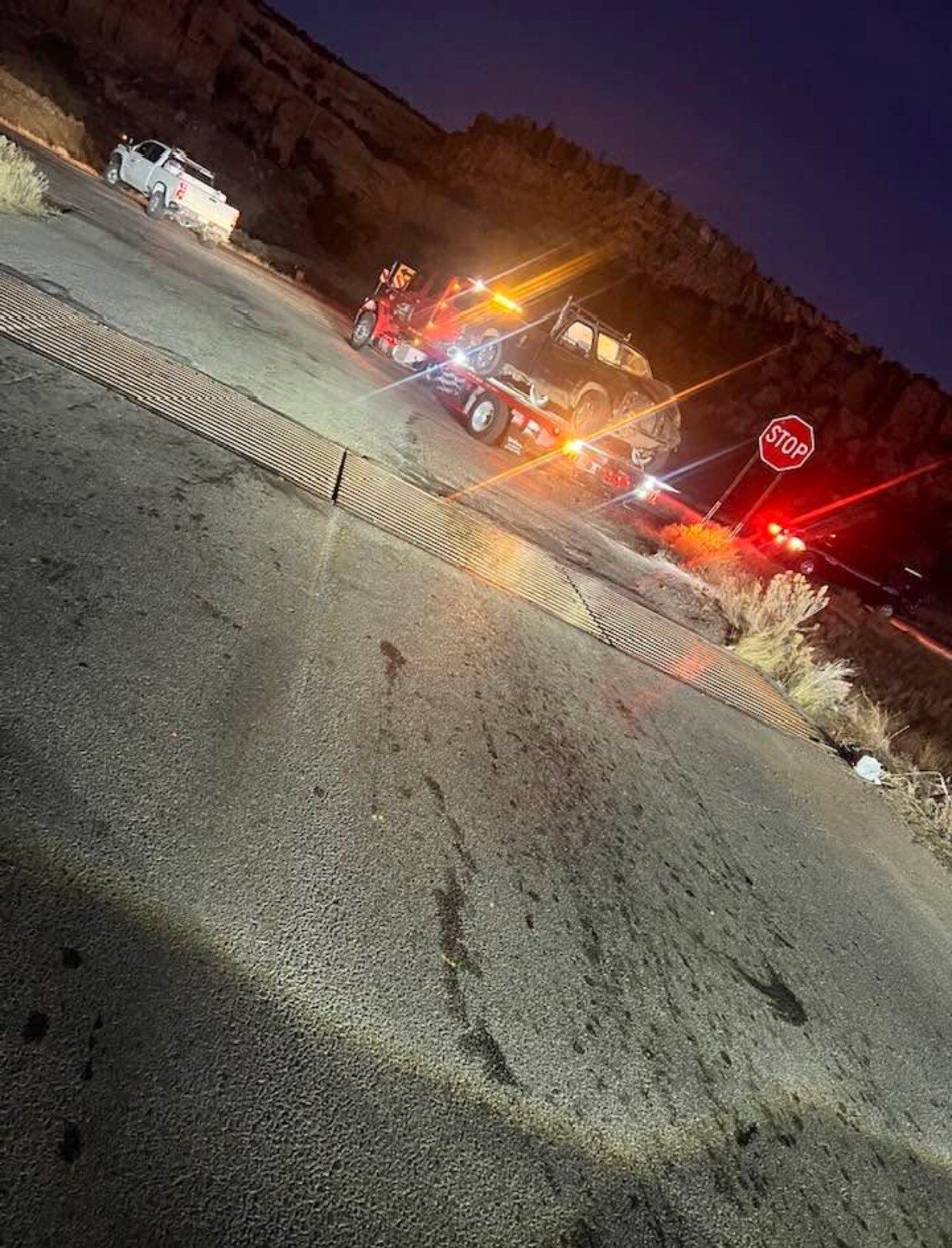 A tow truck is towing a car down a road at night.