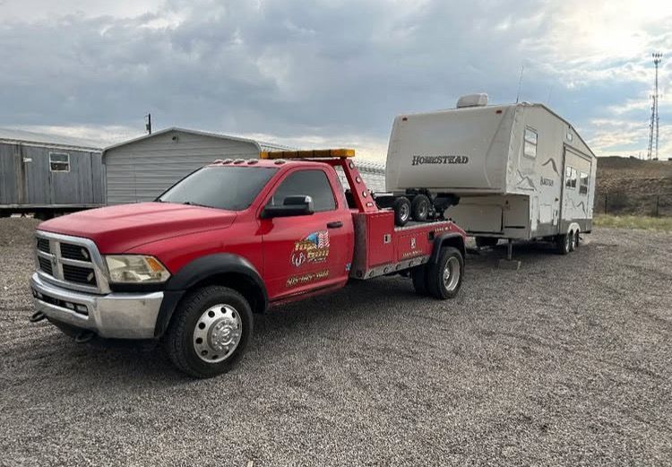 A red tow truck is towing a trailer in a gravel lot.