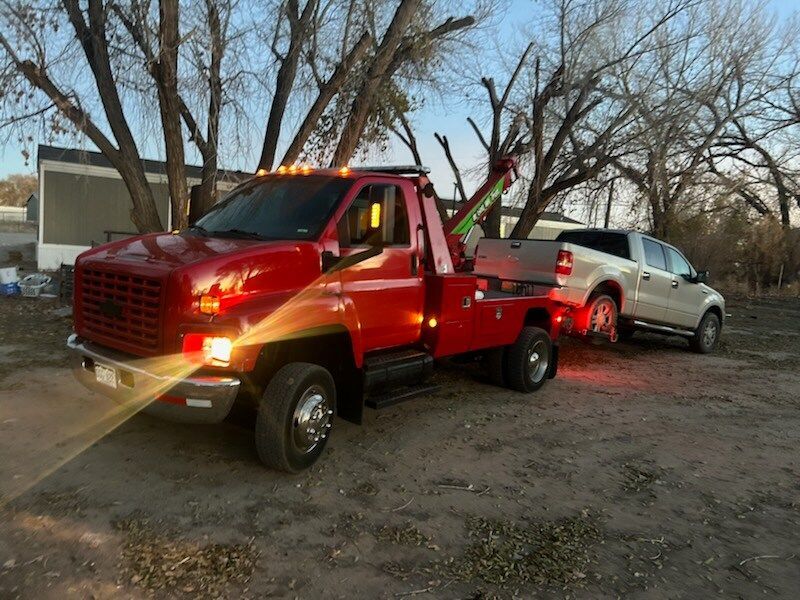 A red tow truck is towing a white truck.