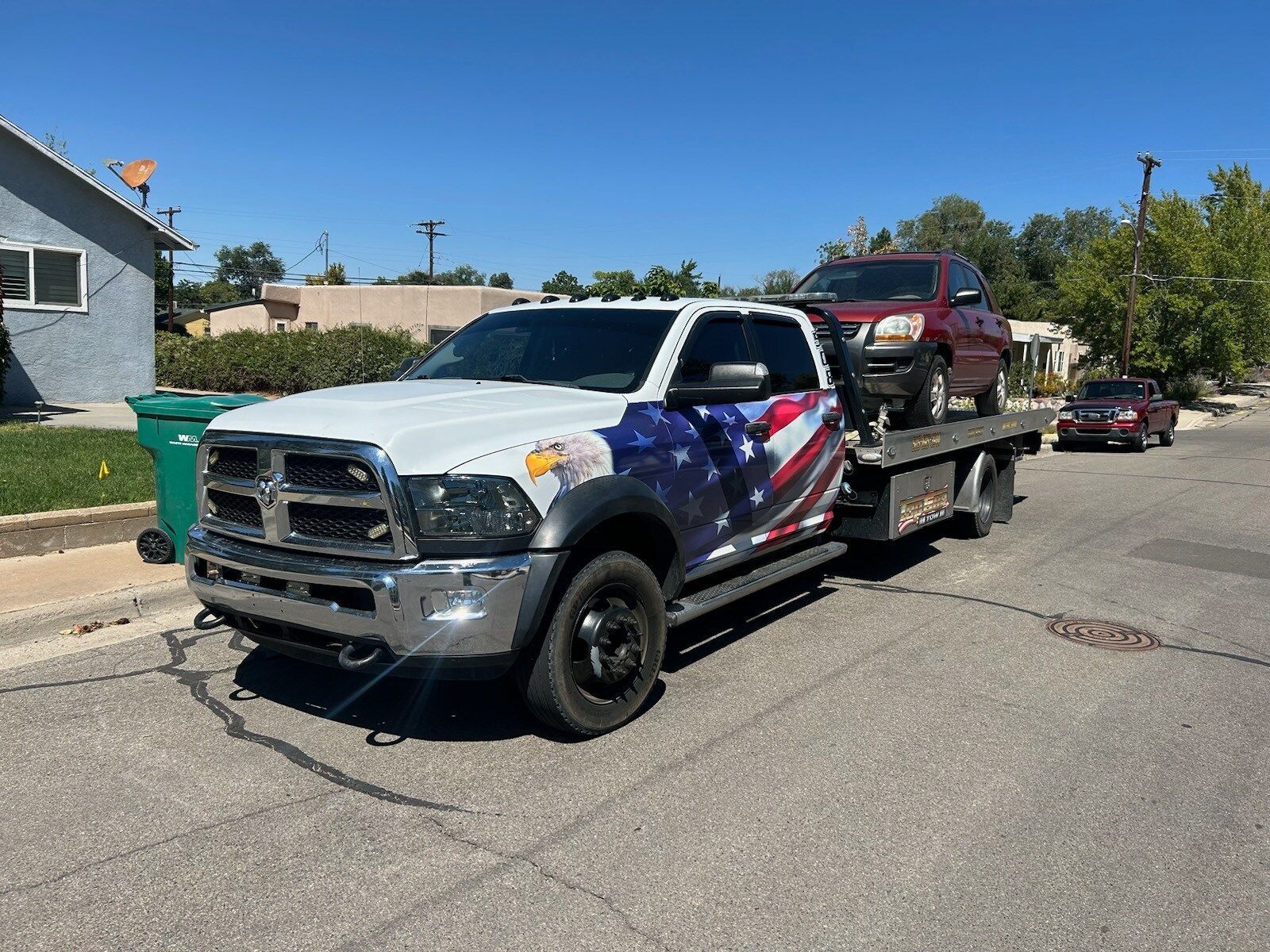 A tow truck with a red car on the back is parked on the side of the road.