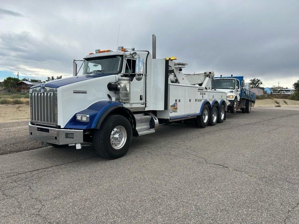 A white and blue tow truck is parked on the side of the road.
