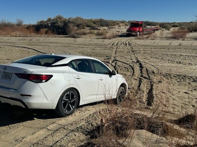 A white car is stuck in the dirt on a dirt road.