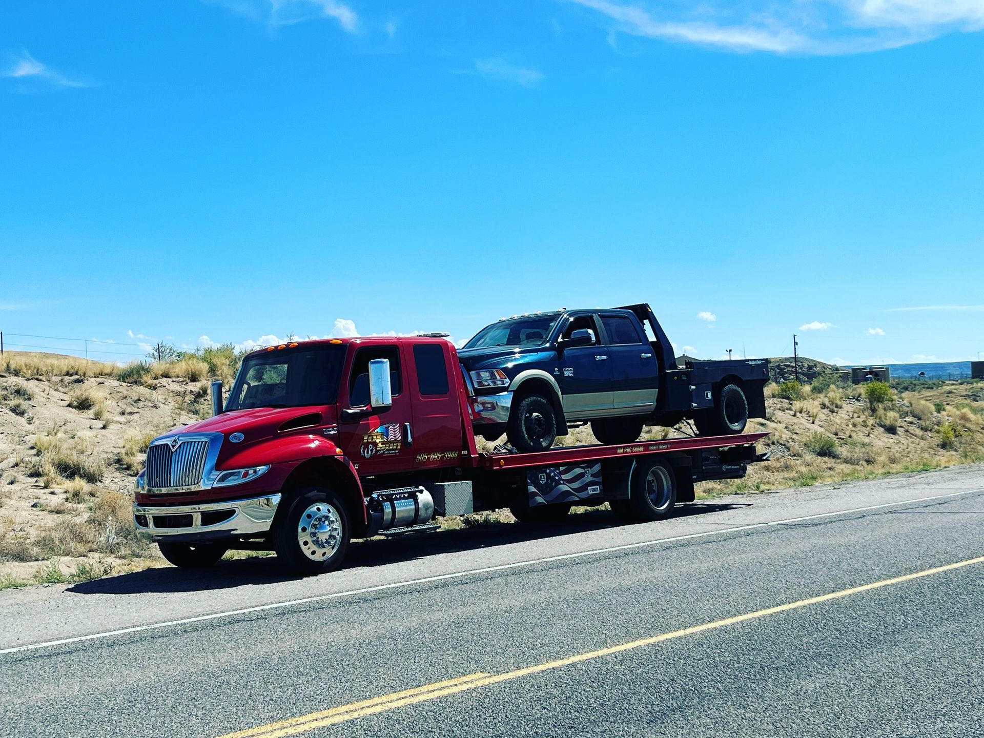 A red tow truck is towing a blue truck down the road.