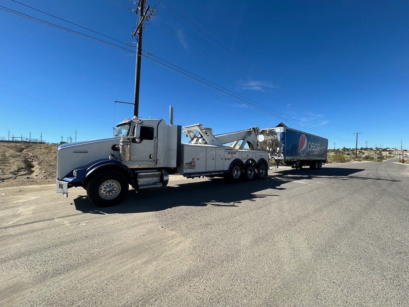 A tow truck with a trailer attached to it is parked on the side of the road.