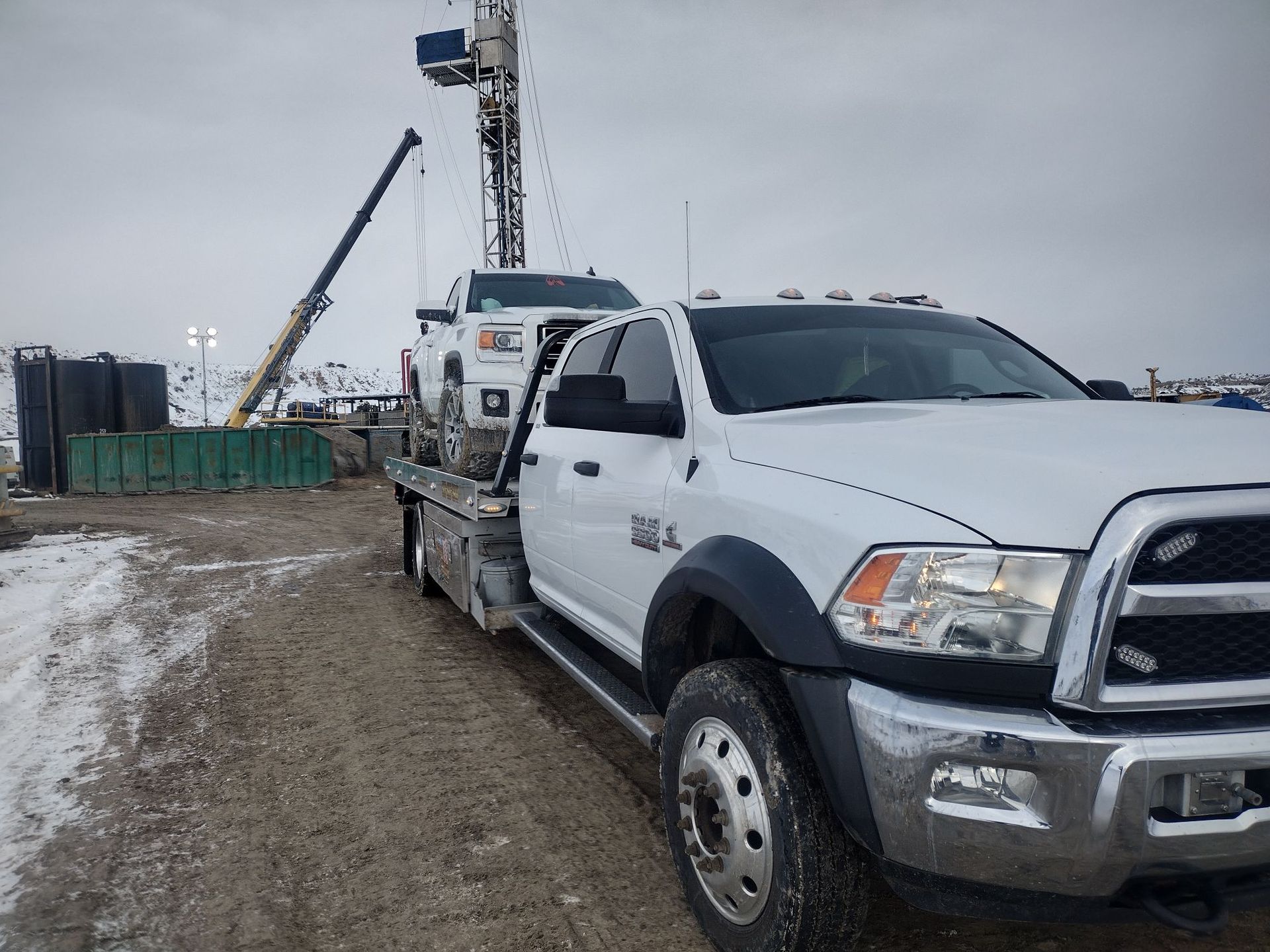 A white truck is parked on a dirt road next to a crane.