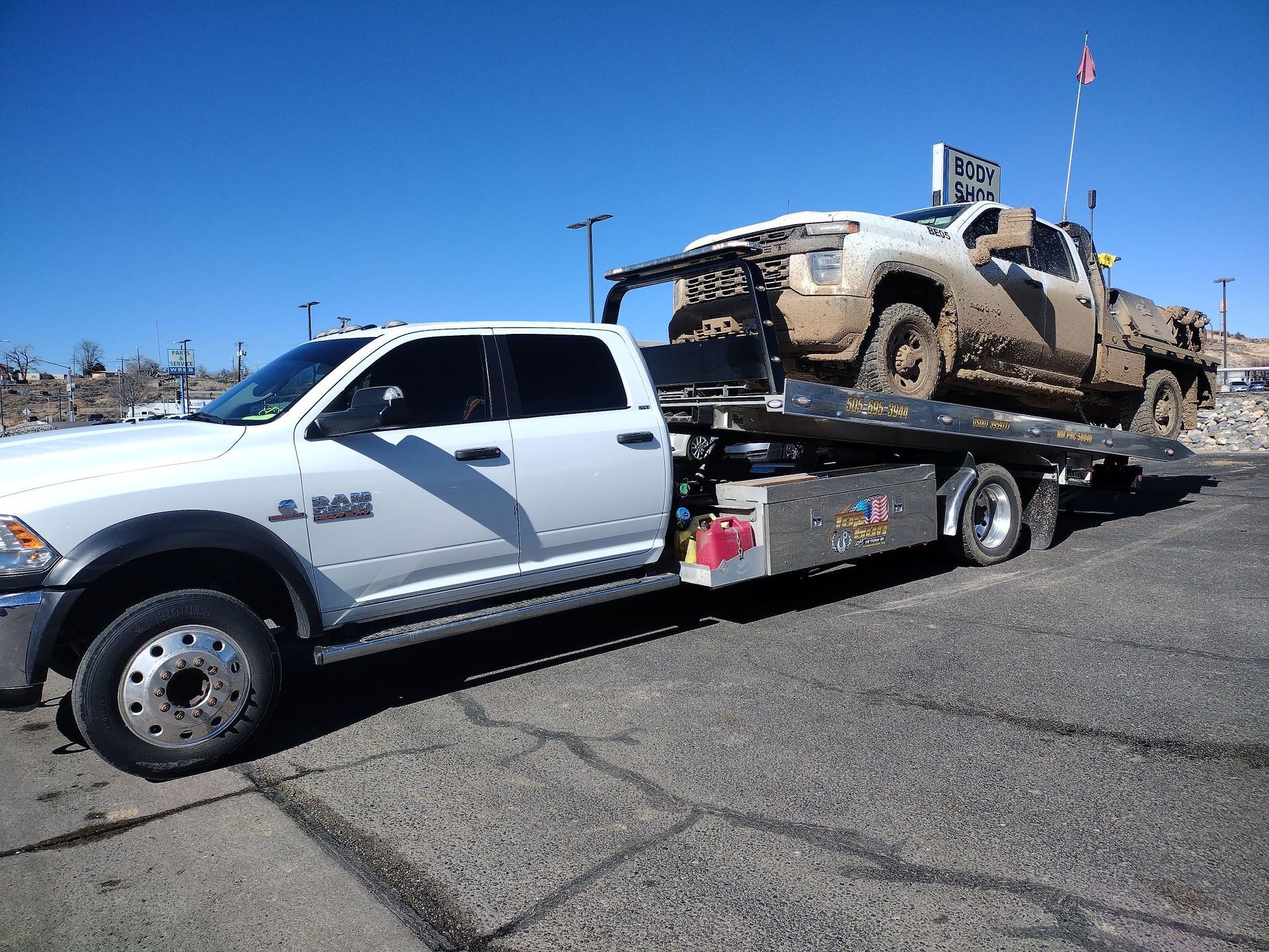 A white truck is towing a muddy truck on a flatbed trailer.