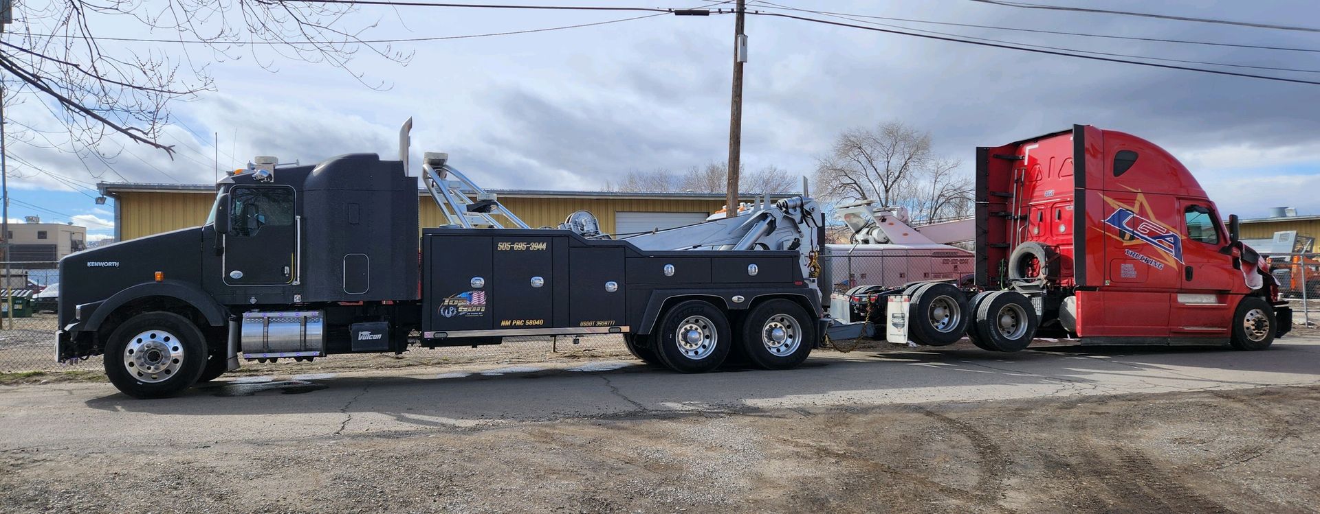 A black tow truck is towing a red semi truck.