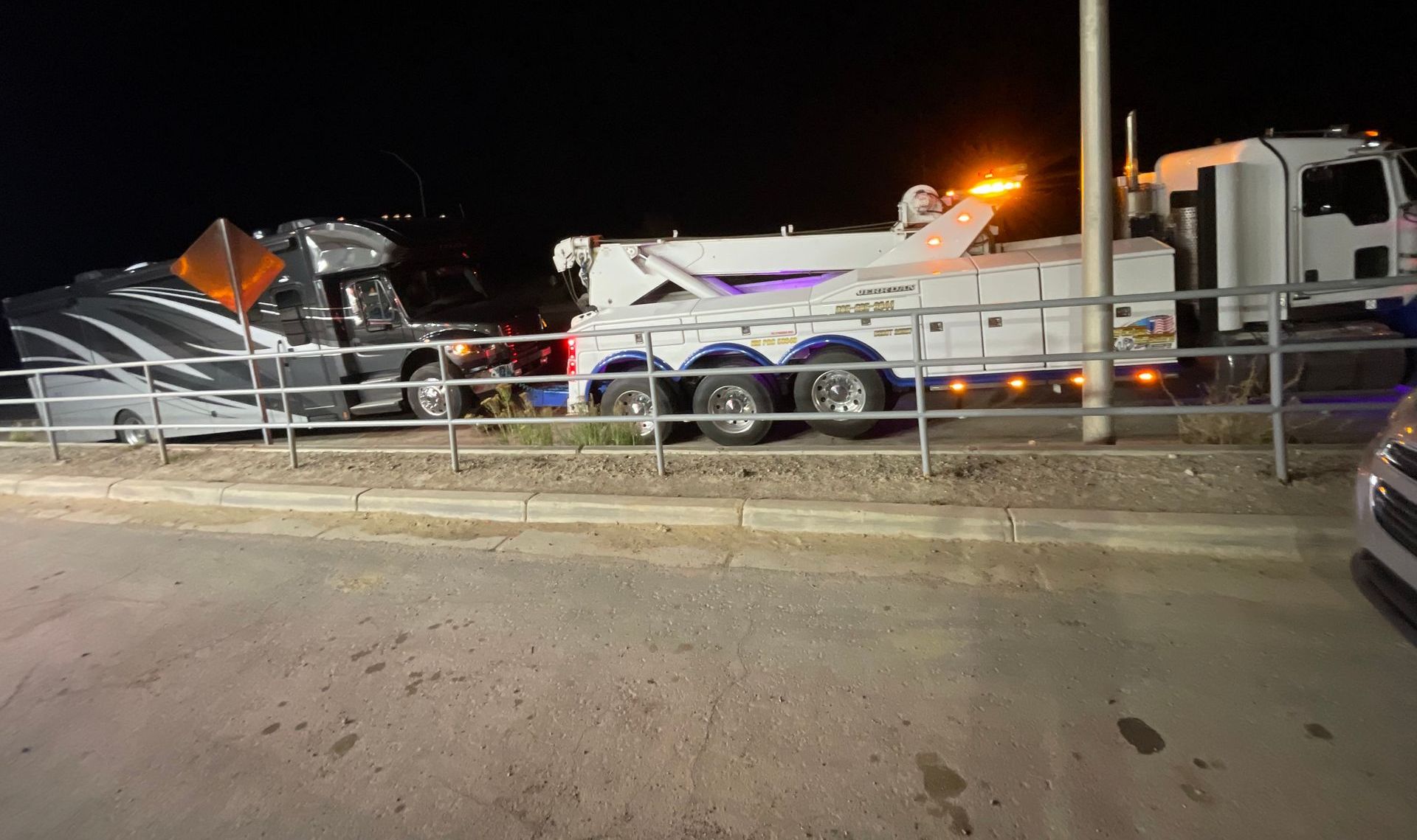 A tow truck is towing a car in a parking lot at night.