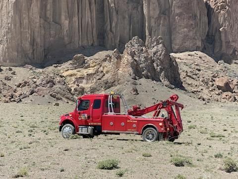 A red tow truck is parked in the middle of a desert.